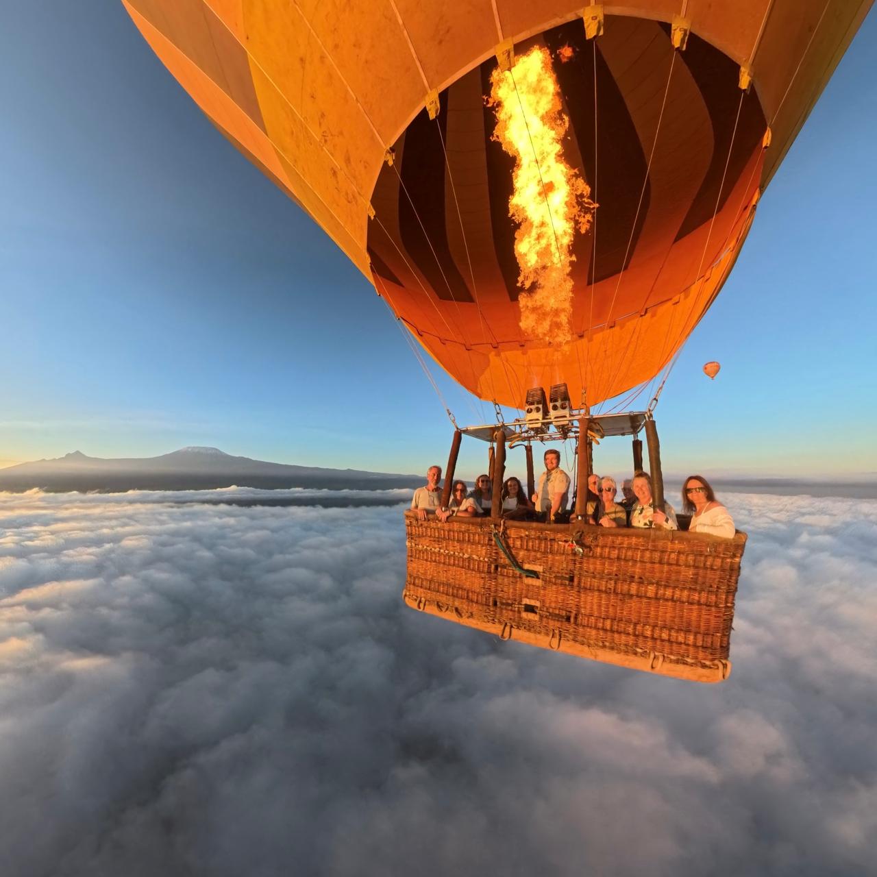 Hot air balloon flying above the clouds at sunrise with Mount Kilimanjaro in the distance